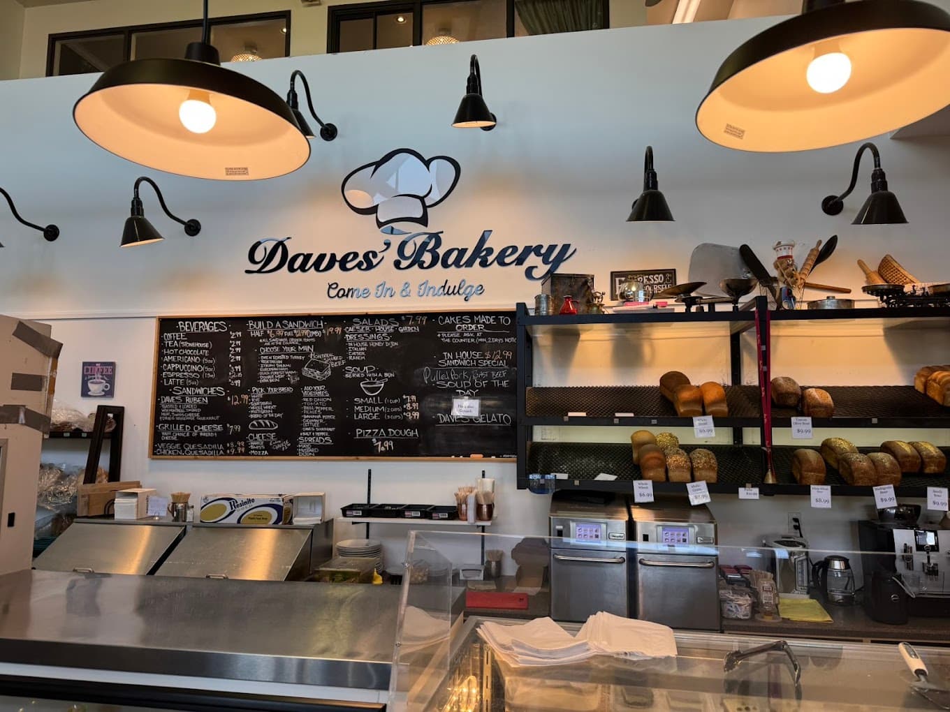 The Daves' Bakery counter: chalkboard menus, bread racks and the painted chef's hat logo