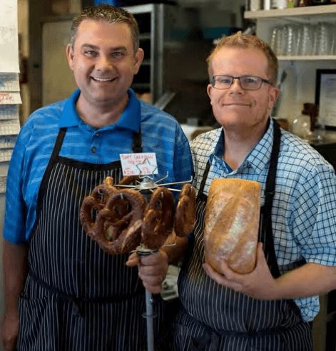 David and Dave in their aprons, holding a stand of soft pretzels and a fresh loaf